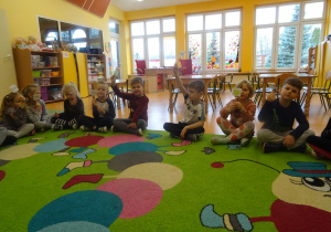 Grupa dzieci siedzi skrzyżnie z uniesionymi tabliczkami z napisem tak, ocenia w ten sposób słuszność zdania wypowiedzianego przez nauczyciela.